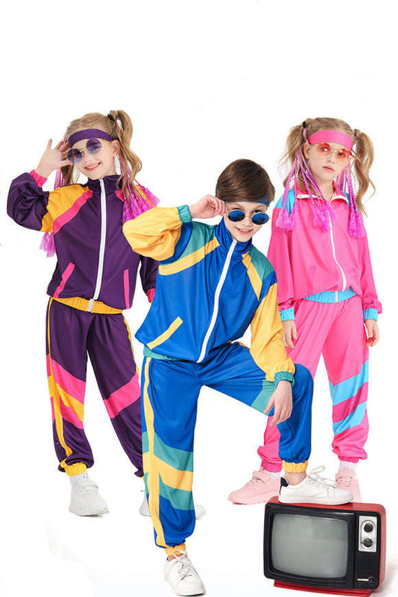 Three children modeling retro 1980s-style colorful tracksuits against a white background, with one child in a blue, yellow, and pink jacket and pants, another in a purple, pink, and yellow jacket and pants, and a third in a pink jacket and pants. They are styled with sunglasses, headbands, and a small vintage television prop.
