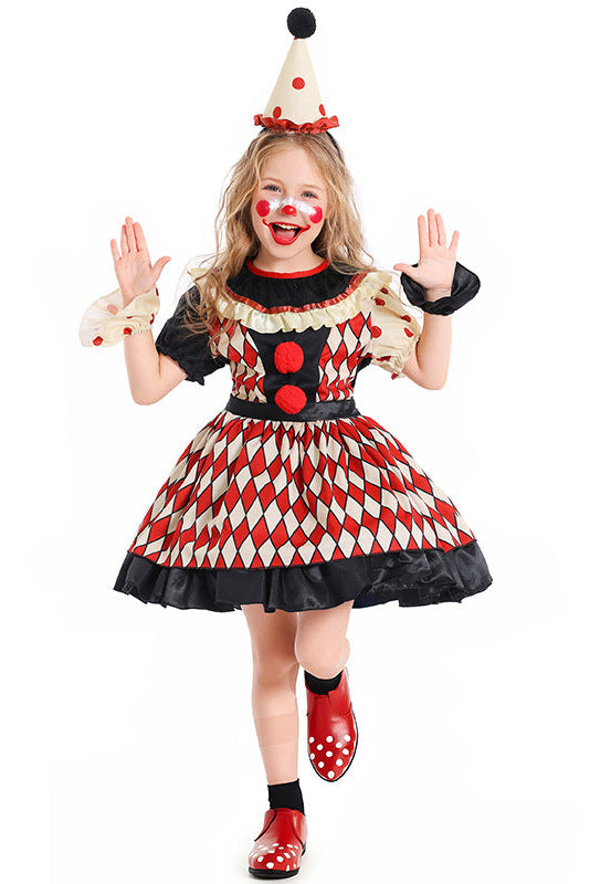 A young girl modeling a clown costume against a plain white background. The costume features a red and cream harlequin patterned dress with black trim, a cream pointed hat with red polka dots and a black pom-pom, red polka-dot shoes, and black socks.