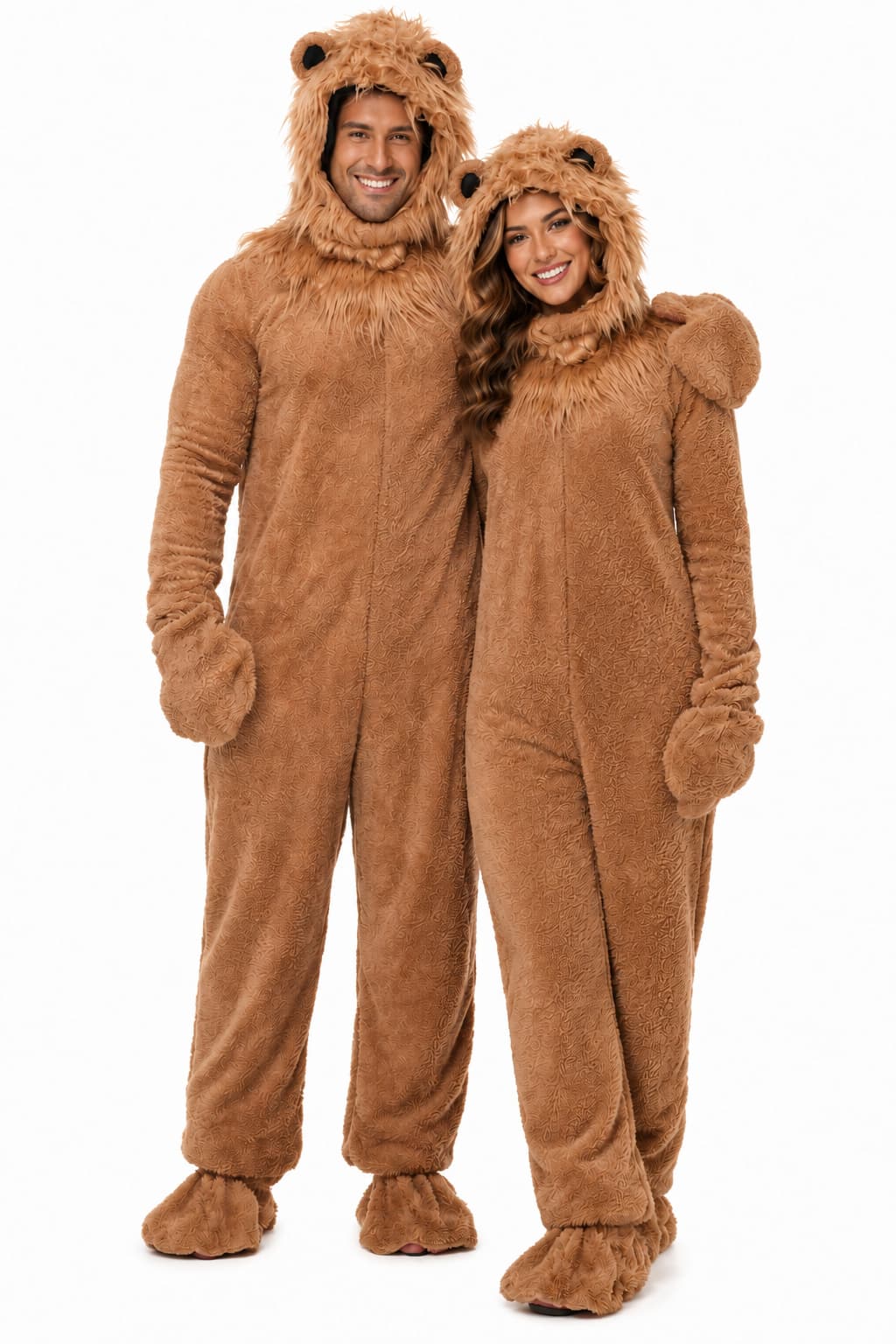 A man and a woman wearing matching brown lion onesies with plush fur-like textures, hooded bear heads, and foot covers, standing against a plain white background.